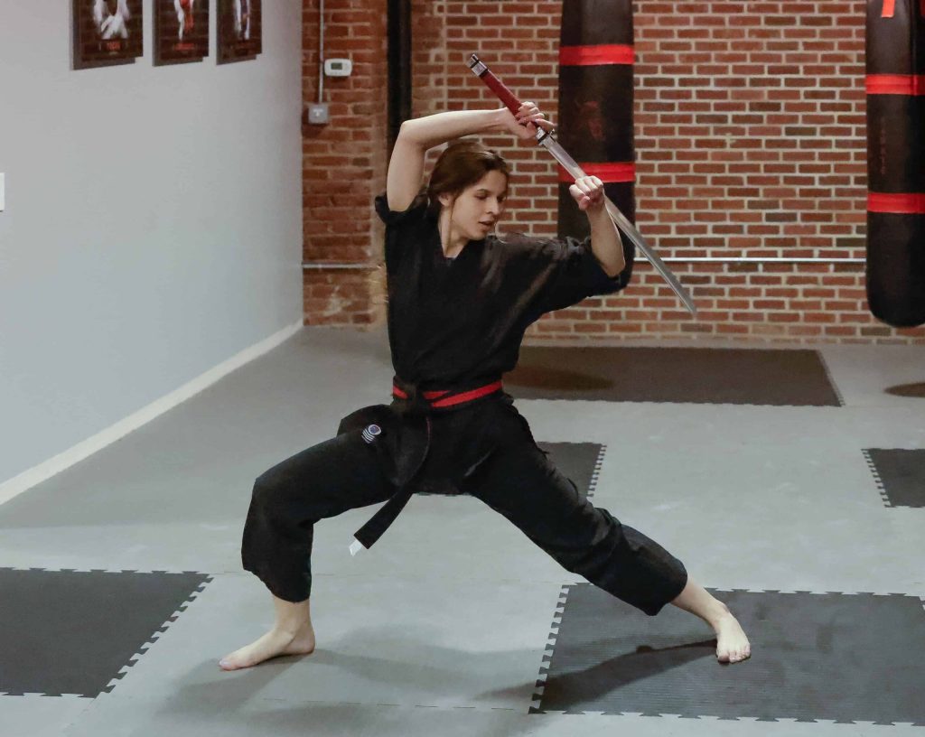 Karate student practicing a sword kata in a martial arts dojo, demonstrating focus, balance, and discipline.
